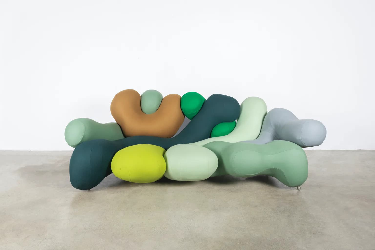 Colorful sculptural furniture installation featuring organic, blob-like forms in muted greens, yellows, browns, and grays by Misha Kahn.