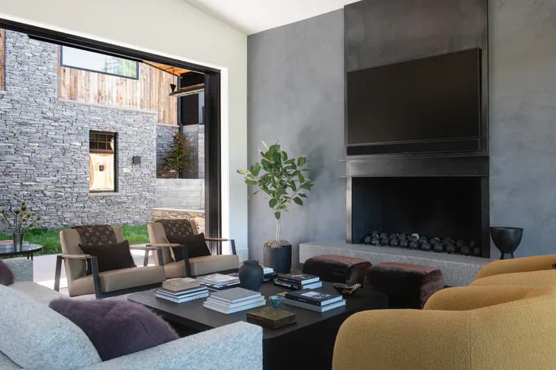 Modern living room with gray concrete fireplace, dark furnishings, and view to stone courtyard, rendered interior by Mo Lebel.