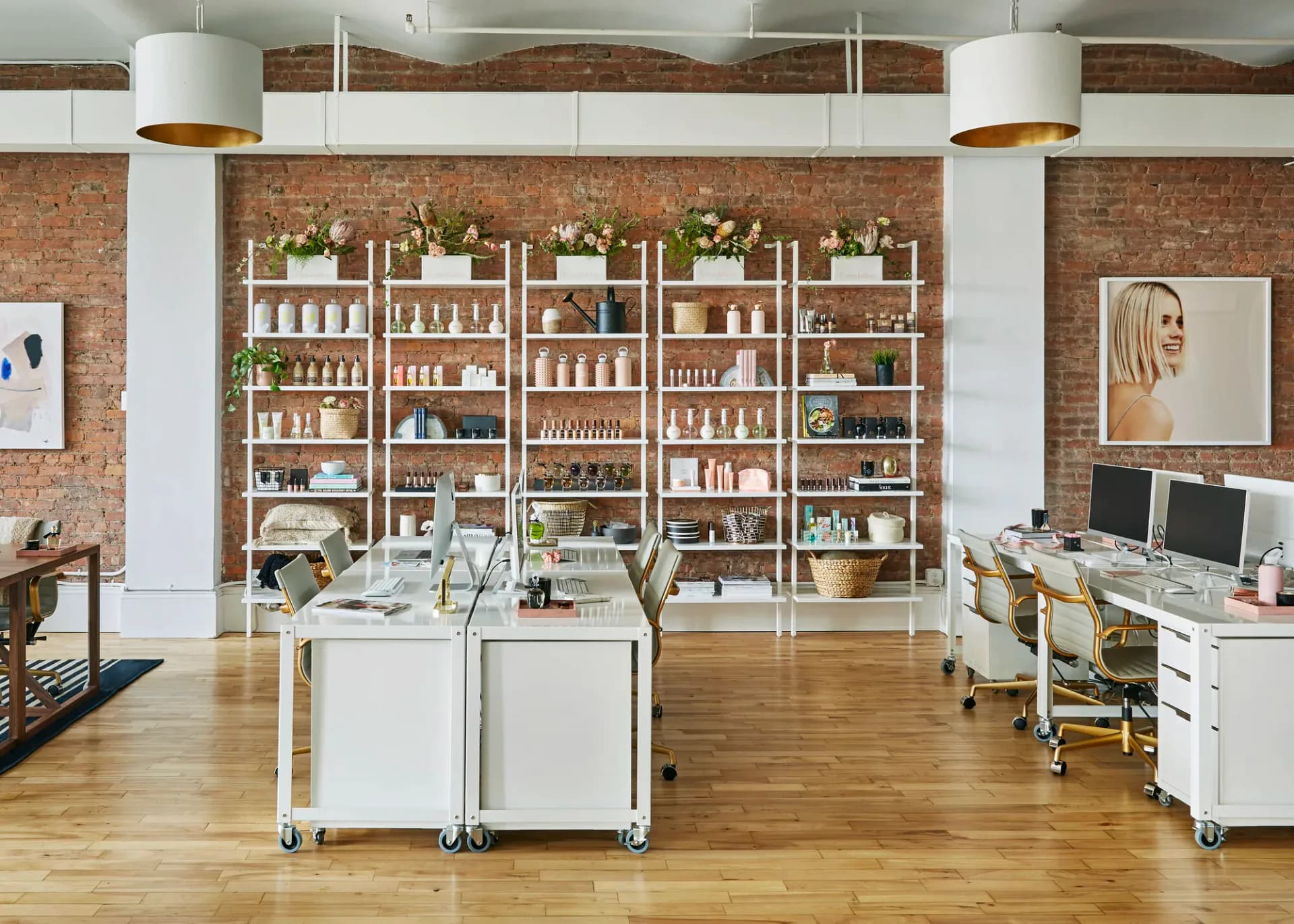 Modern office space with exposed brick walls, white shelving, wooden floors, mobile desks, and pendant lighting by Molly Portnof.