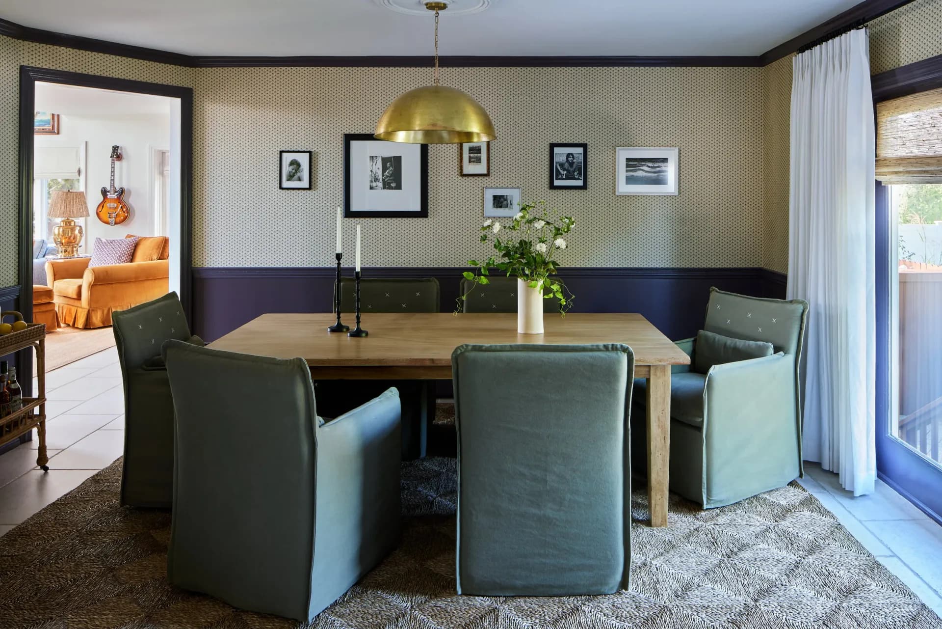 Dining room with banquette seating, wooden table, blue-green upholstered chairs, striped wallpaper, gallery wall, and brass pendant light by Molly Portnof.