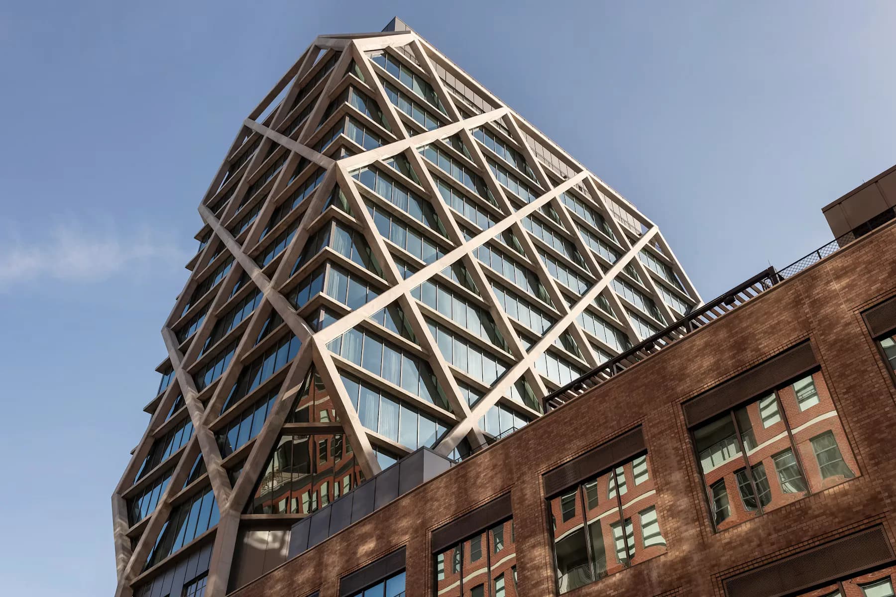 Modern angular glass and steel tower structure with dramatic diagonal lattice framework rising above a red brick historic building, designed by Morris Adjmi.