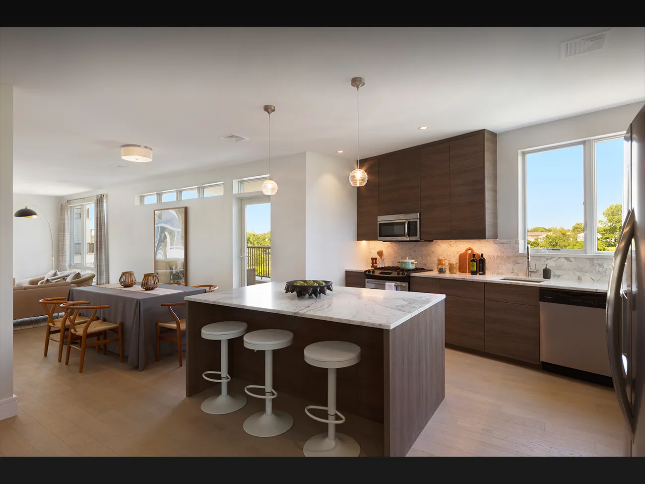 Modern kitchen and dining area with dark wood cabinetry, white quartz island, stainless steel appliances, and large windows overlooking landscape by Nancy J. Ruddy.