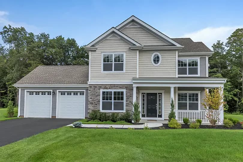 Two-story colonial-style house with gray siding, stone accents, gabled roofline, two-car garage, and manicured lawn by Nancy Zito.