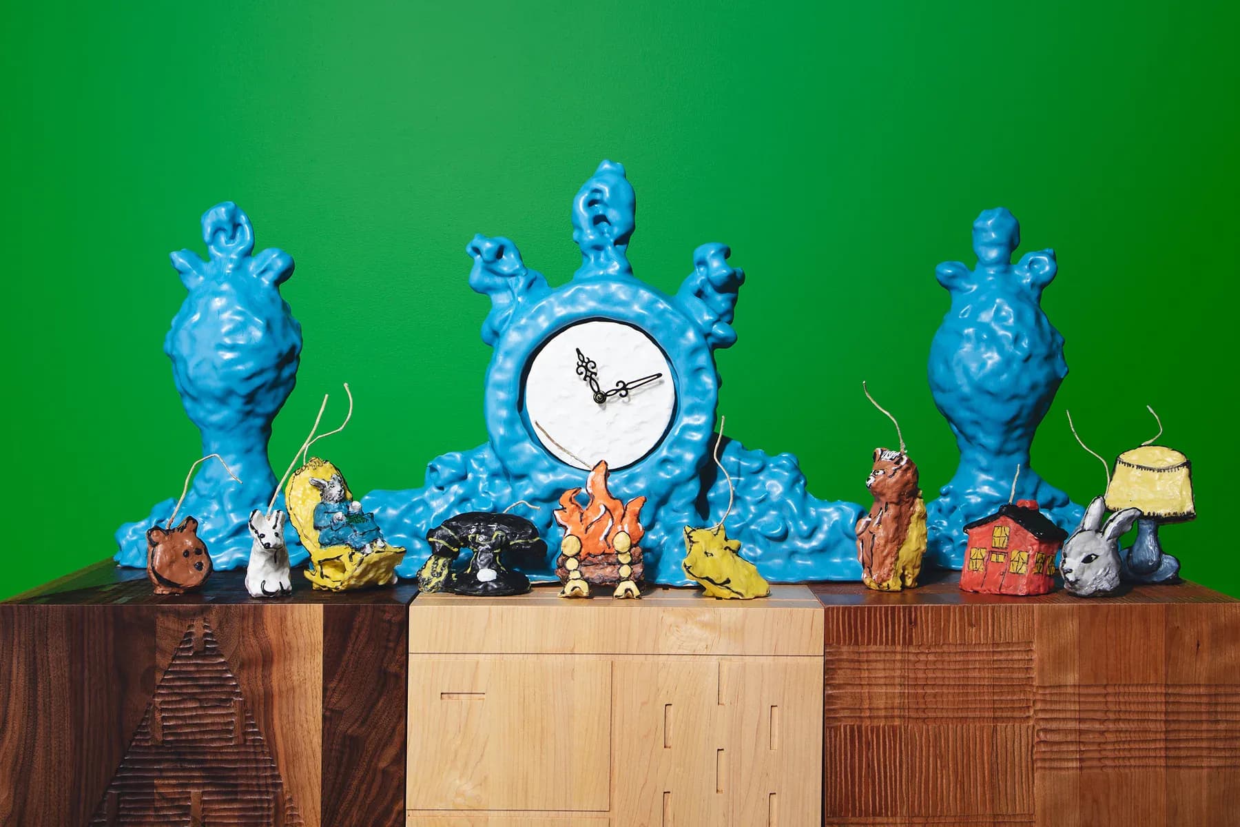 Styled shelf display featuring blue ceramic vessels, decorative objects, and a central clock against a green wall, wooden cabinetry by Naomi Clark.