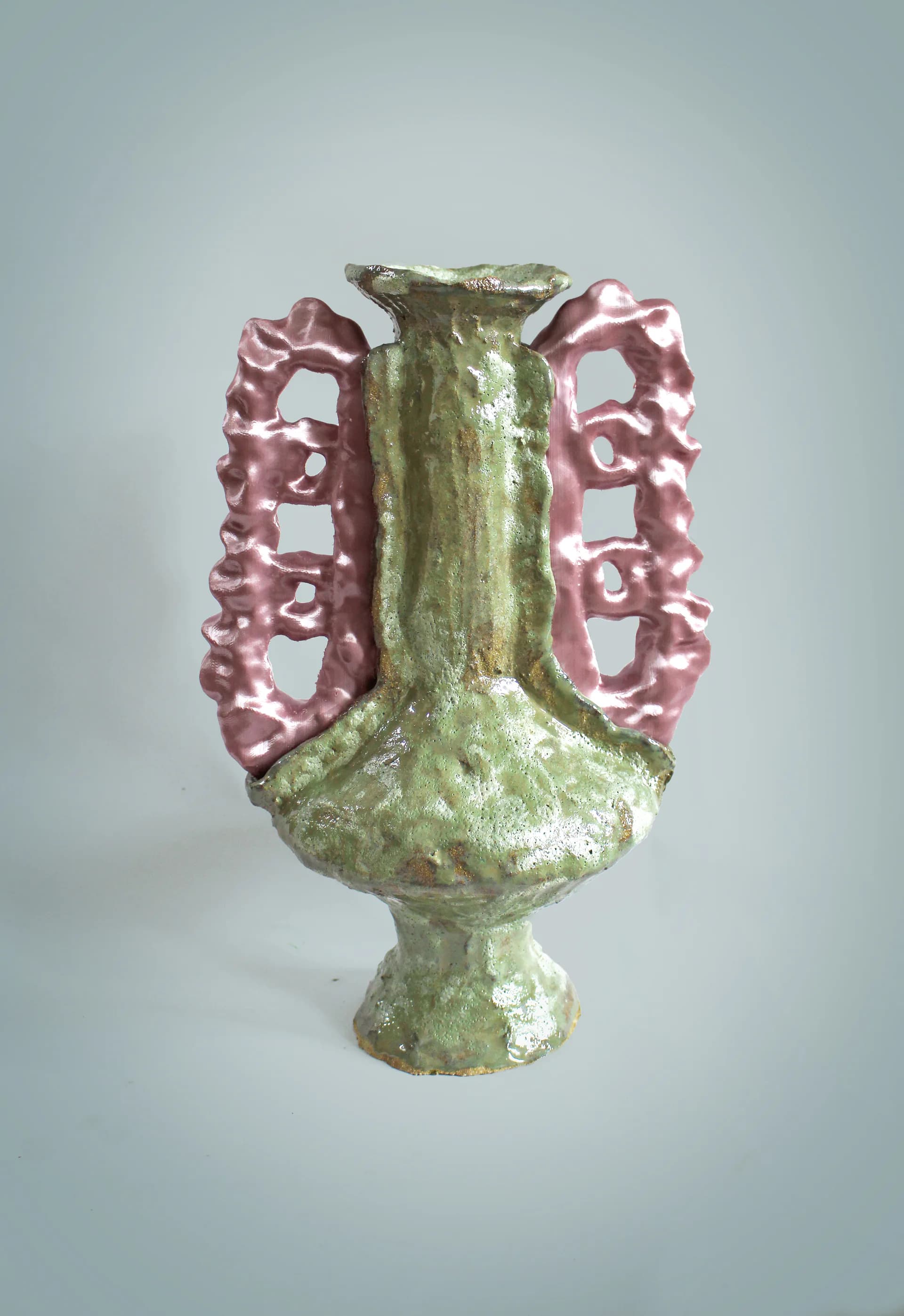 Sculptural ceramic vessel with green glazed central column and dual pink metallic handles featuring geometric cutout patterns, by Natalia Triantafylli.