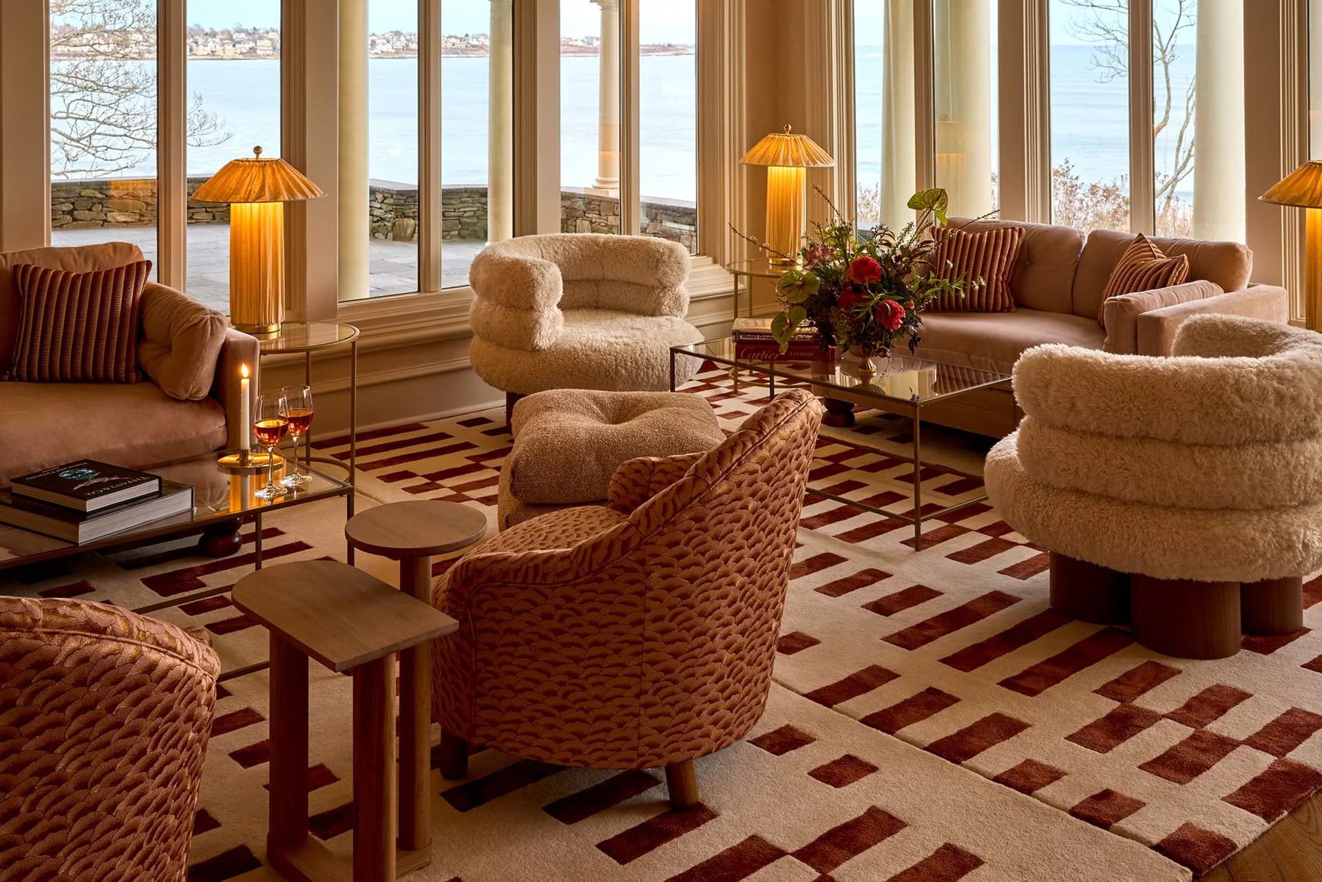 Luxury living room with warm neutral tones, plush curved seating, geometric patterned flooring, and floor-to-ceiling windows overlooking a landscape by Natalie Imran.