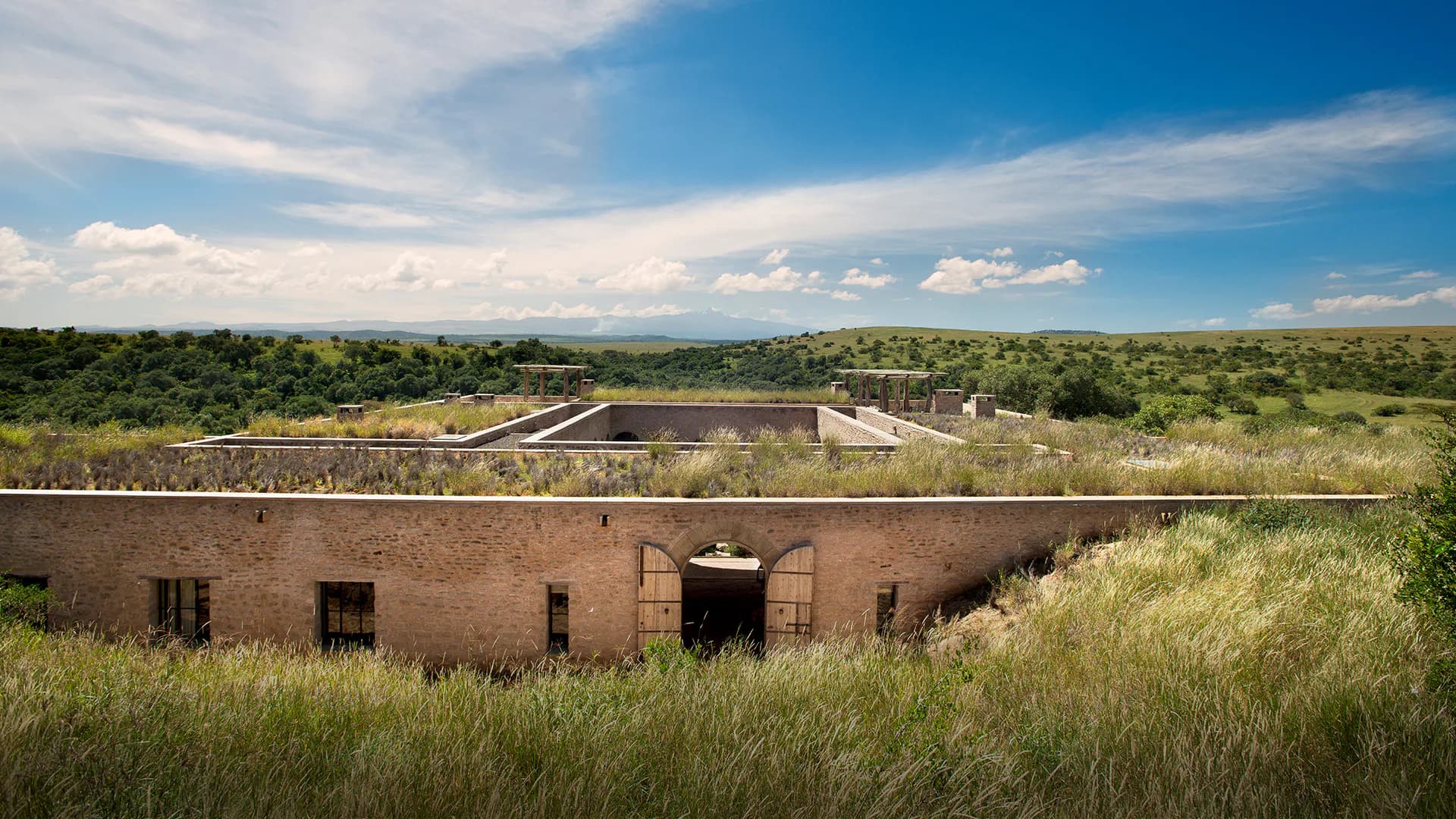 Earthen fortification with brick construction set in expansive savanna landscape with native grasses and distant tree line by Naushin Rahman.