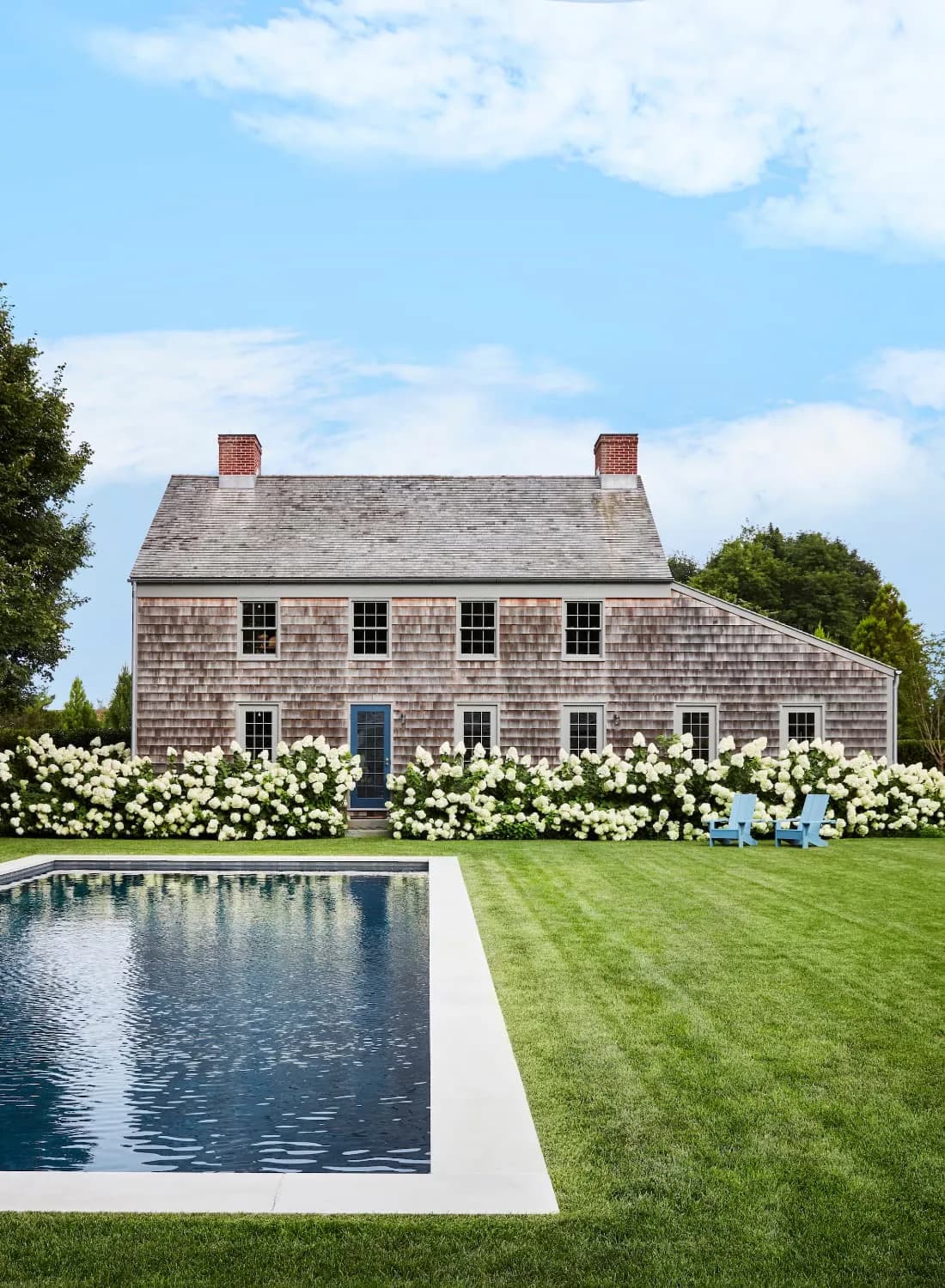 Modernist shingle-clad residential home with symmetrical facade, manicured lawn, white hydrangeas, and rectangular reflecting pool by Neal Beckstedt.
