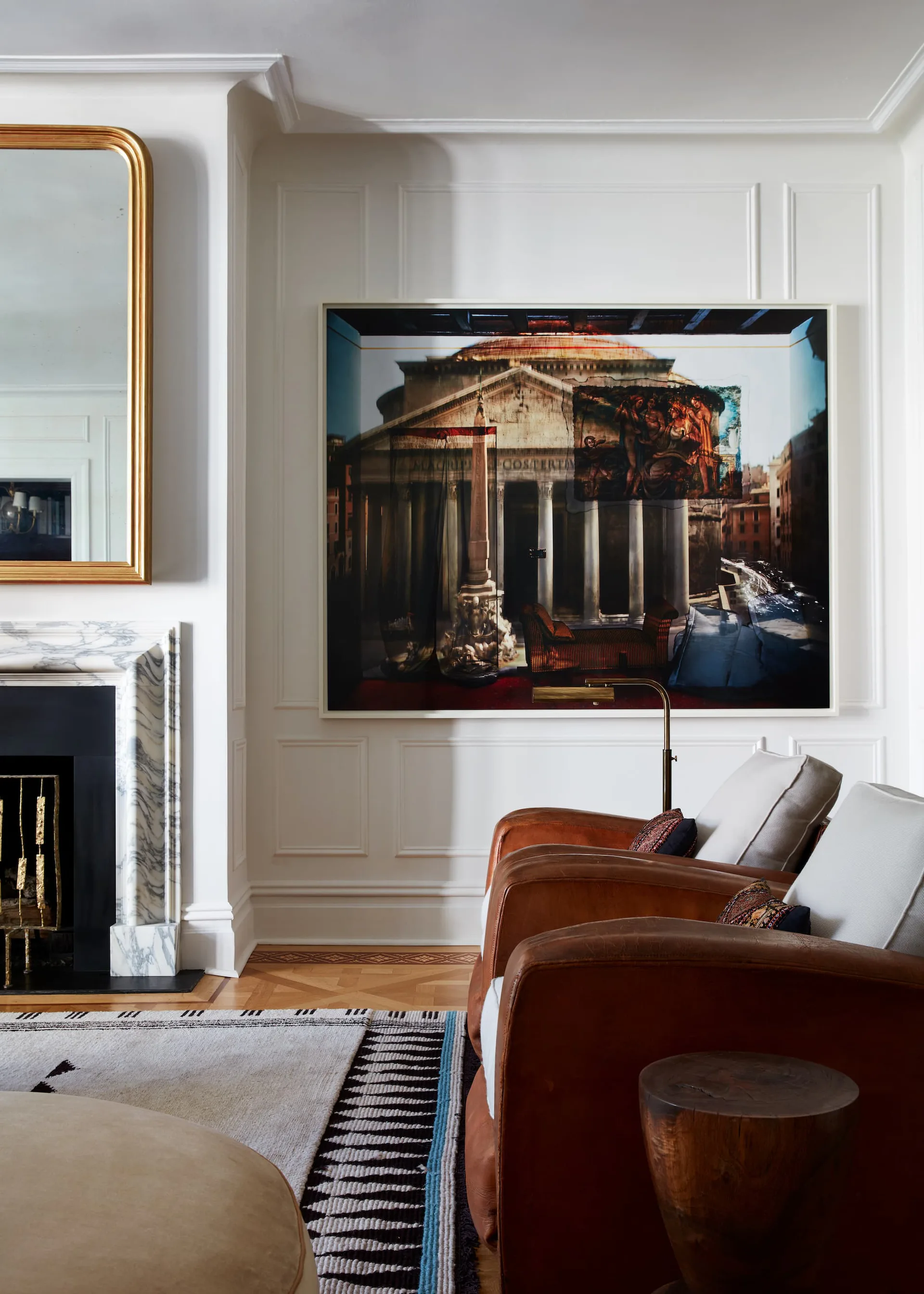 Elegant living room with cognac leather armchair, fireplace with gold mirror, and large framed architectural photograph on white paneled wall by Neal Beckstedt.
