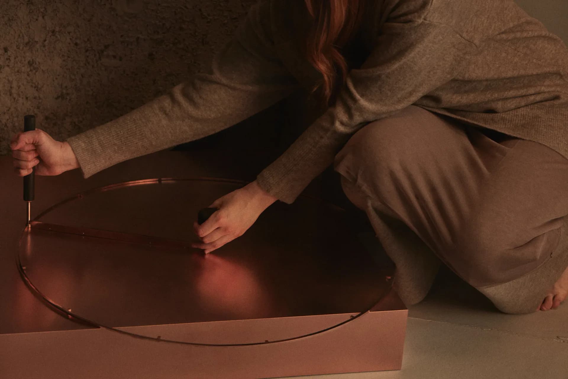 Designer's hands manipulating a curved architectural model or installation element against warm, ambient lighting, showcasing material exploration by Nel Verbeke.