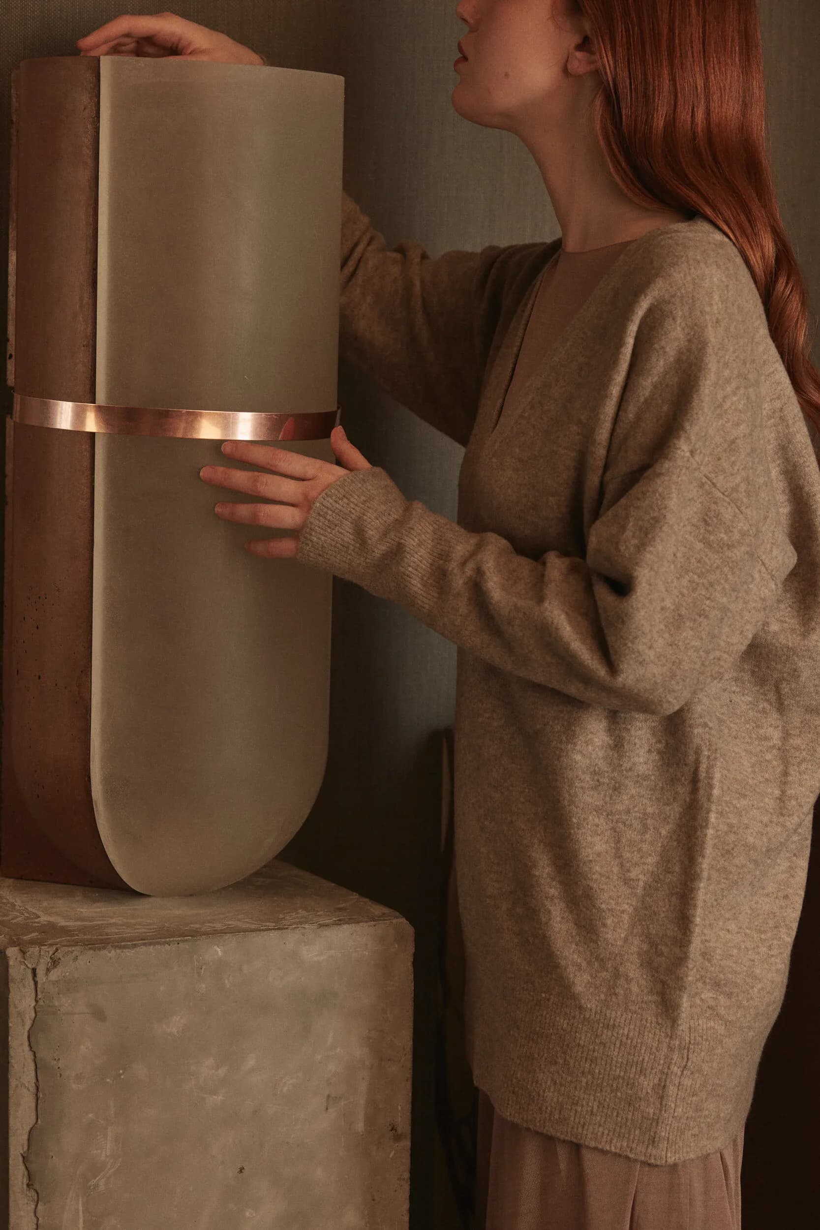 Tall cylindrical sculptural vessel in cream with copper band detail, displayed on concrete plinth by Nel Verbeke.