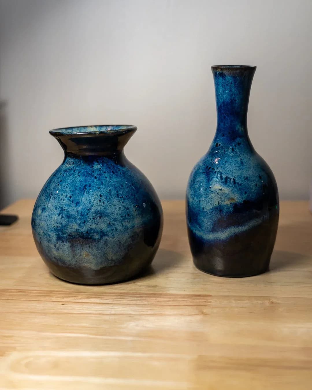 Two blue and black ceramic vessels with textured glazed surfaces displayed on a wooden surface by Nicholas Talamo (WorksbyNET).