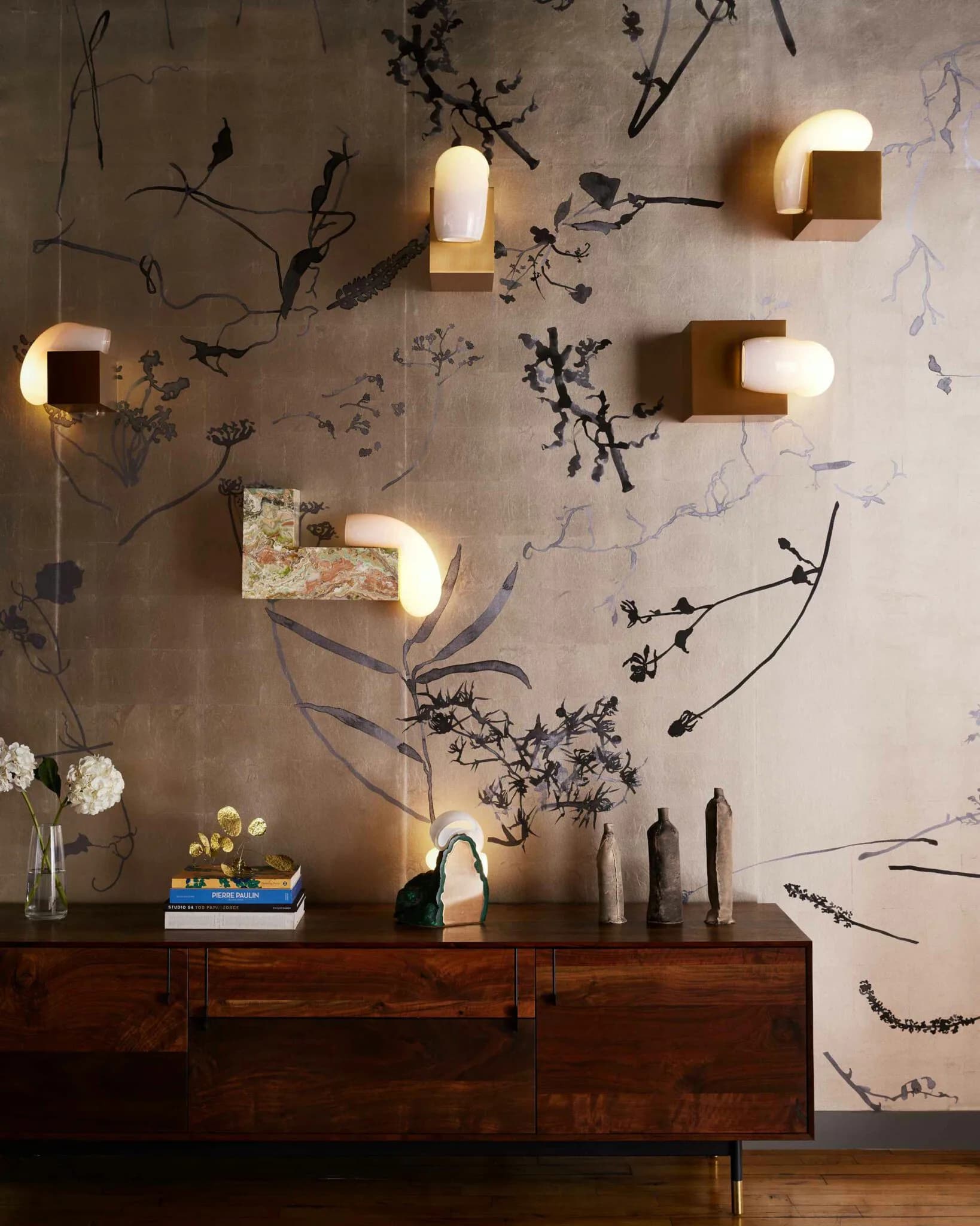 Modern interior wall installation featuring botanical line-art murals with integrated wooden shelving units and warm-toned pendant lighting by Nick Cope.