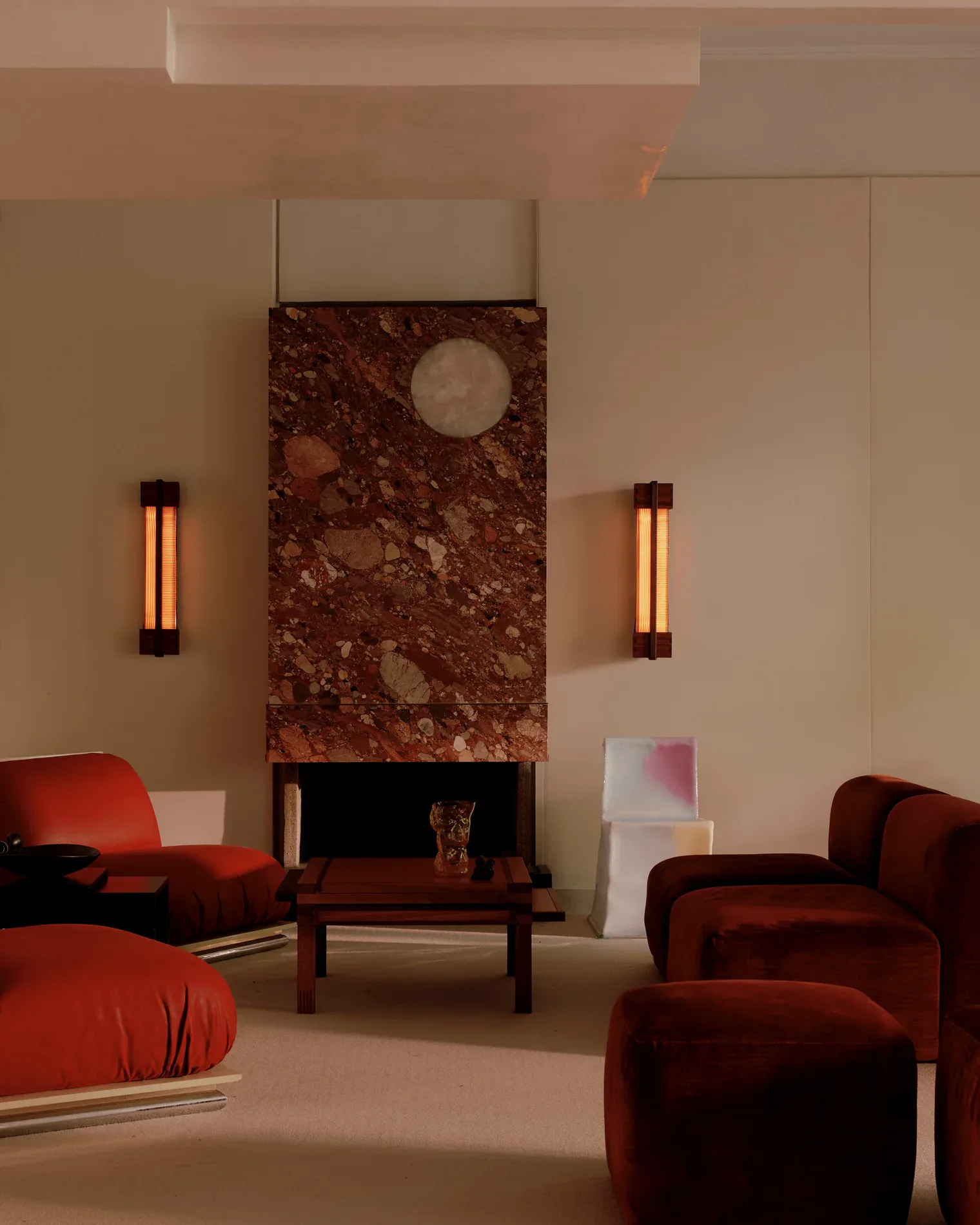 Luxurious living room with burgundy velvet furniture, a striking red marble fireplace surround, vertical brass sconces, and warm taupe walls by Nick Ozemba.