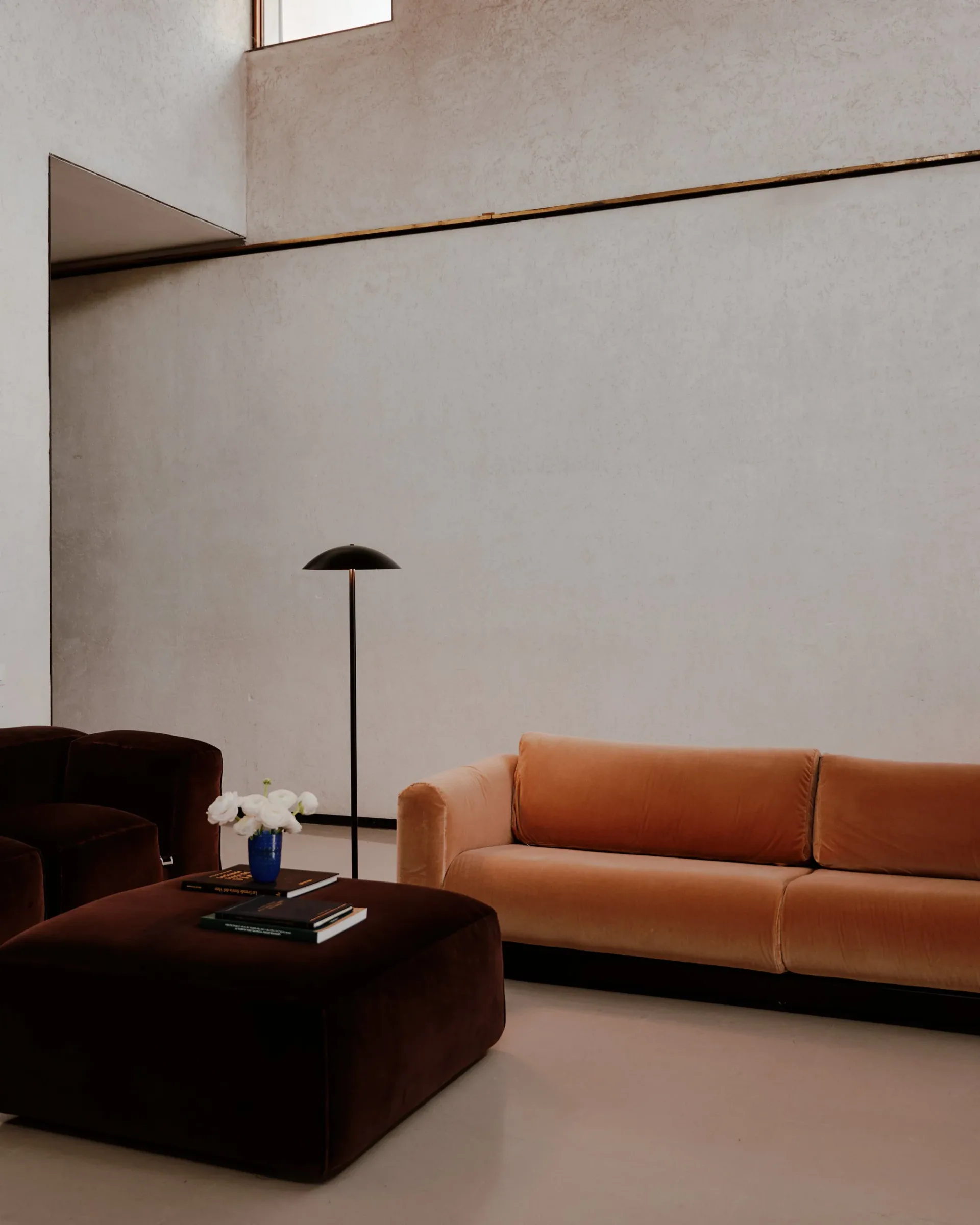 Minimalist living room with cognac leather sofa, dark brown curved chair, black arc floor lamp, and high white walls with angular architectural details by Nick Ozemba.