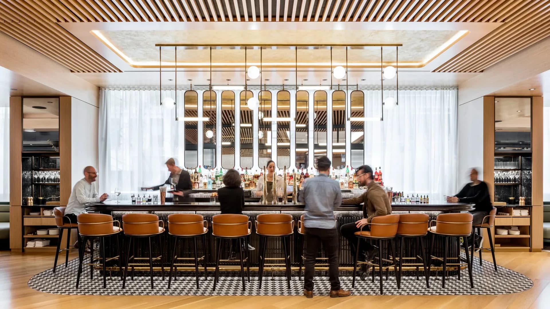 Modern bar interior with wood ceiling details, geometric pendant lighting, and orange leather seating by Nicolas Martin.