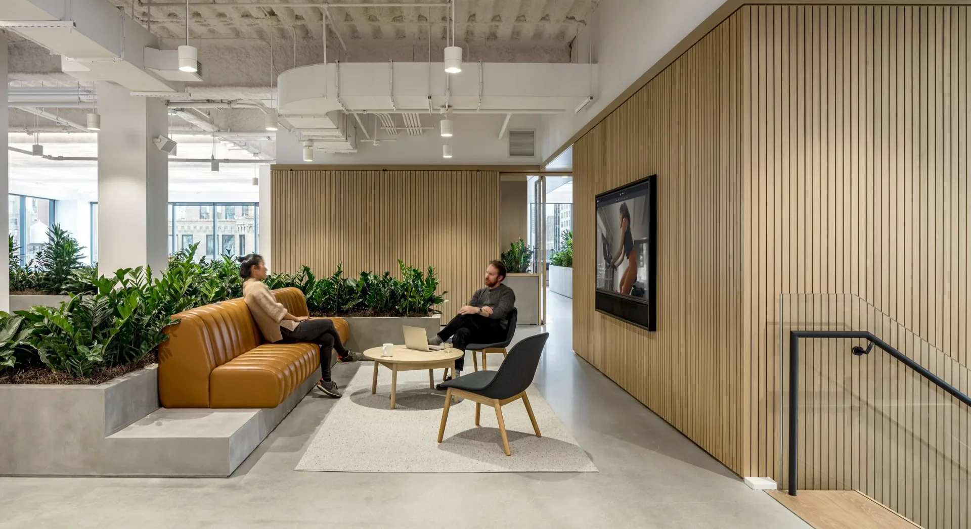 Modern office lounge with mustard-yellow ribbed sofa, wood-paneled accent wall, potted greenery, and minimalist furnishings by Nicolas Martin.