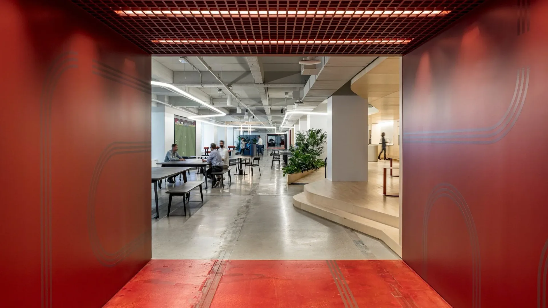 Modern office space with red accent walls, polished concrete flooring, and industrial ceiling details, designed by Nicolas Martin.