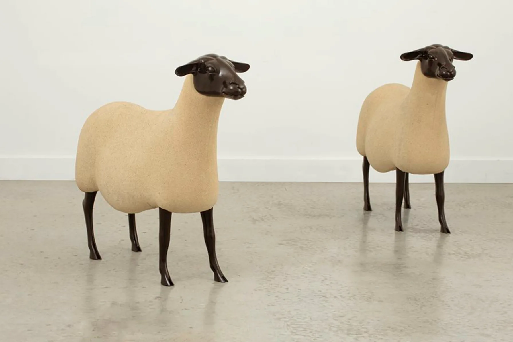 Two sculptural sheep figures with cream-colored woolly bodies and dark bronze heads and legs positioned in a minimalist gallery space by Nicole Fuller.