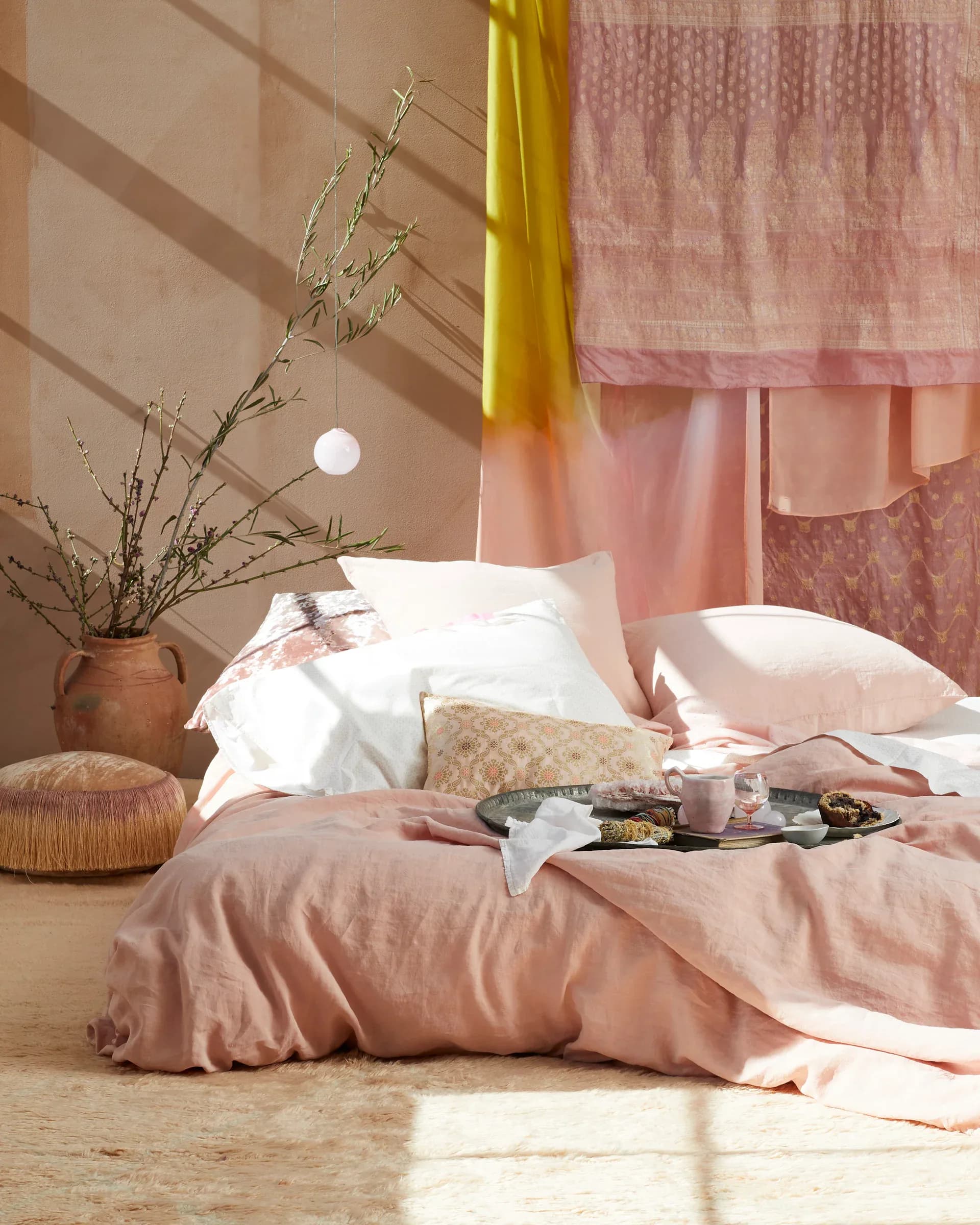 Serene bedroom with pink and neutral tones, white pillows, linen bedding, dried botanicals in terracotta vase, and soft natural light by Nicole Pierpont.