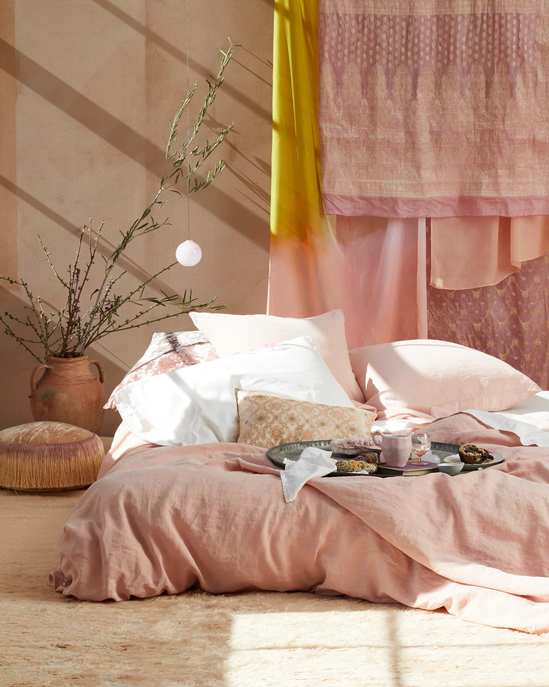 Serene bedroom interior with blush pink bedding, white pillows, natural wood accents, dried botanicals, and warm neutral palette designed by Nicole Pierpont.
