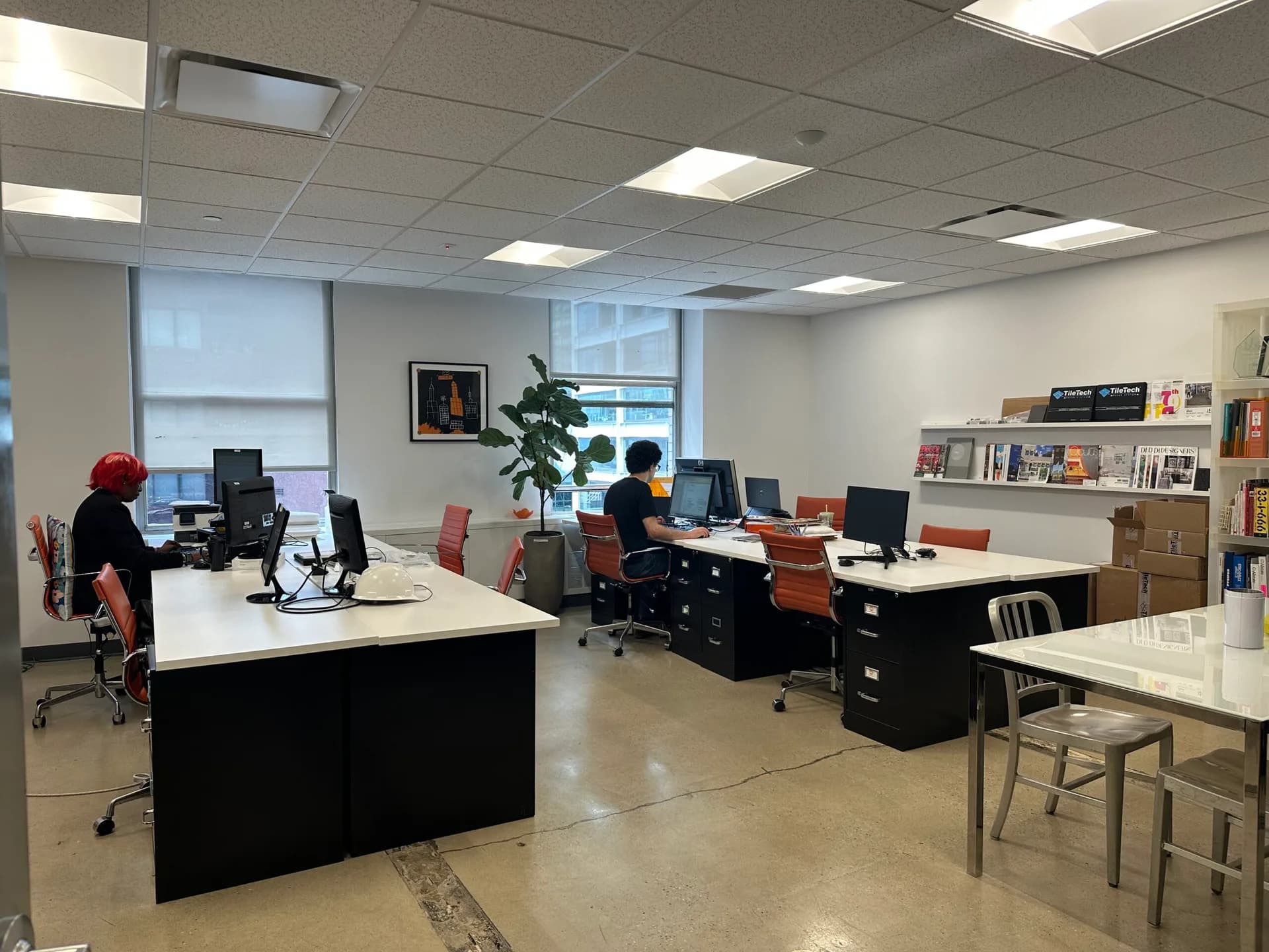 Modern office space with white desks, orange chairs, wooden storage units, and large windows, designed by Nicole Robertson.