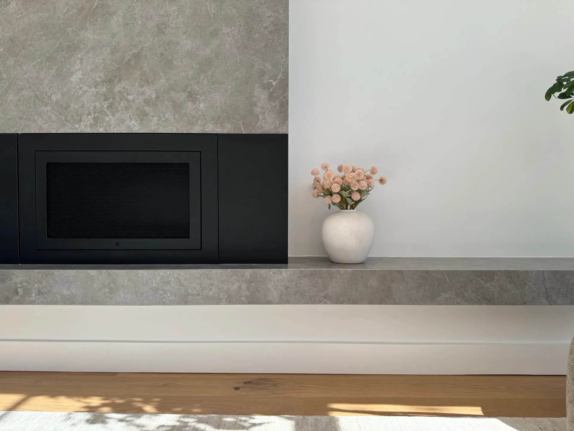 Minimalist interior with concrete and white walls, black media console, white shelf displaying coral flowers in ceramic vase by Nina Fisher.