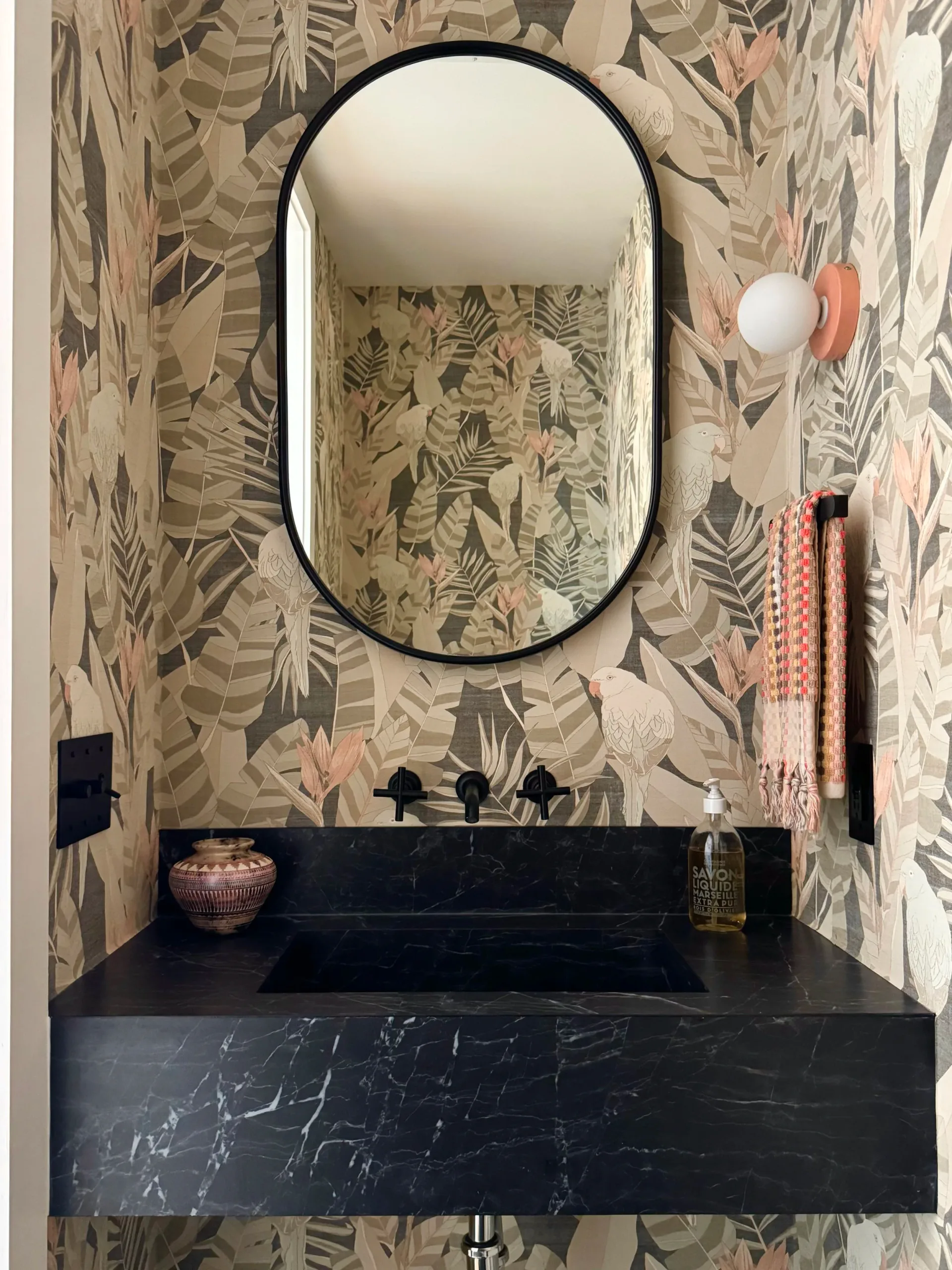 Black marble bathroom vanity with oval mirror and botanical wallpaper in muted tones, designed by Nina Fisher.
