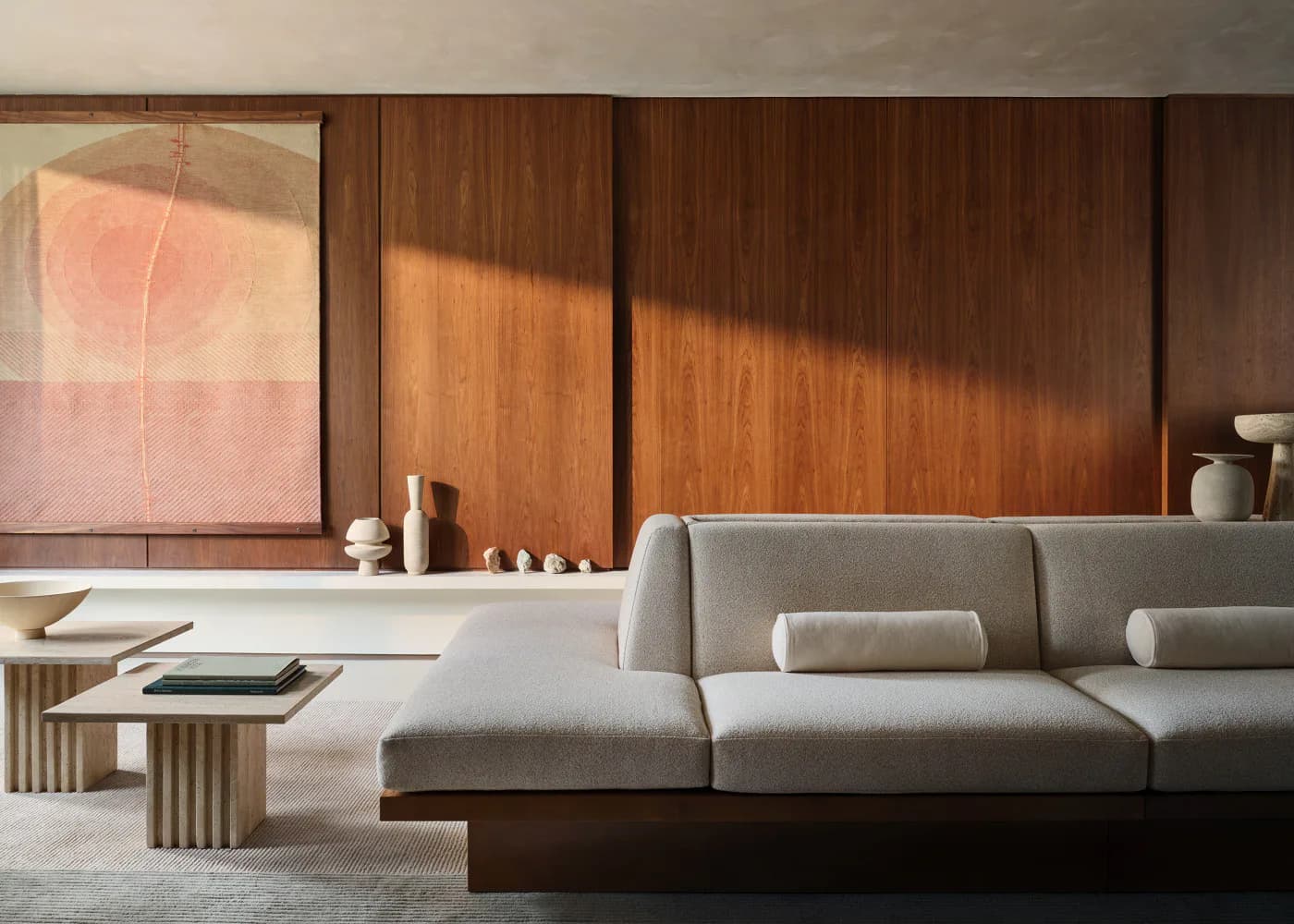 Minimalist living room with gray sectional sofa, warm wood paneling, and soft natural lighting casting shadows on walls, by Nina Jakic.