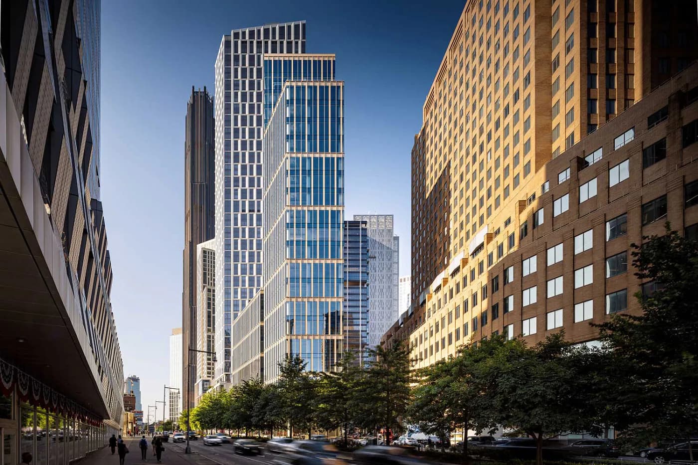 Modern urban street canyon with contemporary glass and metal skyscrapers, tree-lined plaza, and clear blue sky, designed by Nina Jakic.