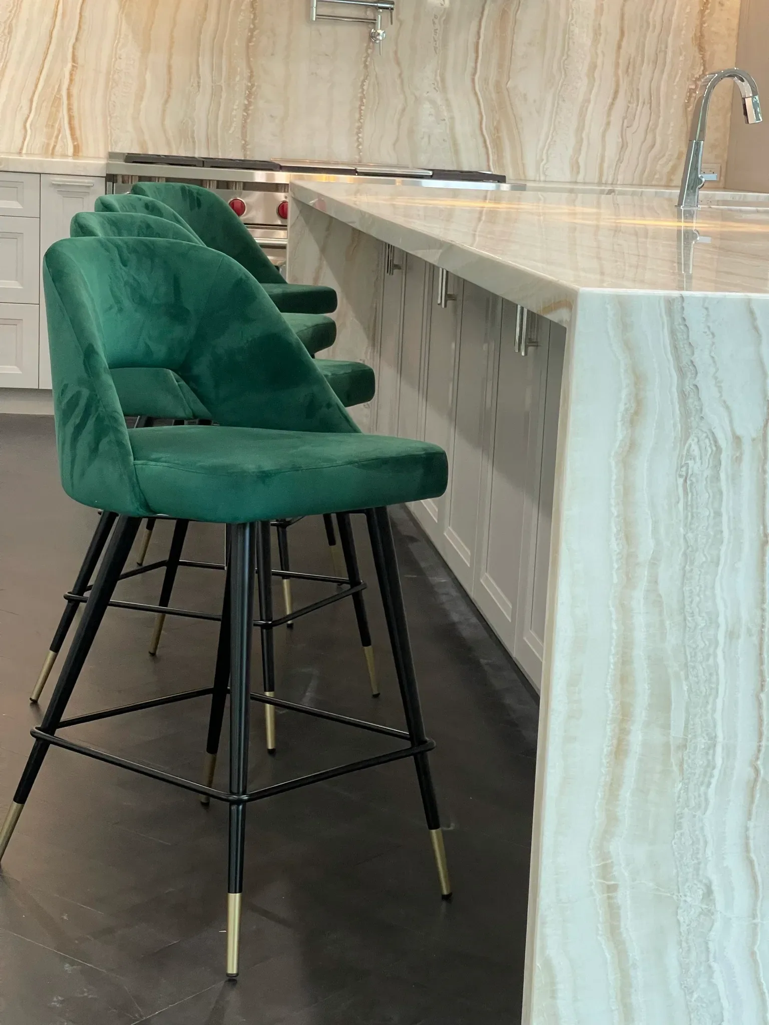 Modern kitchen island with green velvet bar stools and black metal legs, paired with light marble countertop and waterfall edge by Nina Nielsen-Norwood.