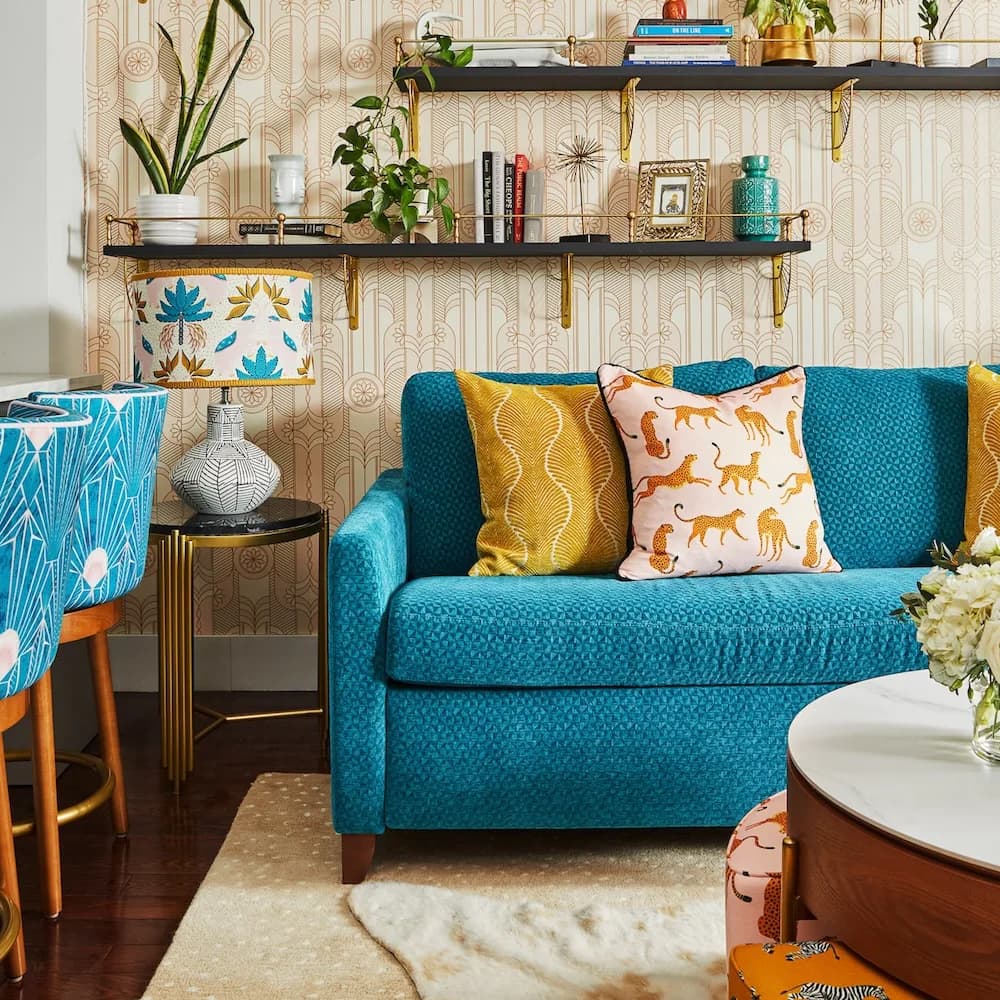 Eclectic living room with turquoise upholstered sofa, patterned throw pillows, floating wooden shelves with potted plants, and warm wood paneling by Nivi Ravi.