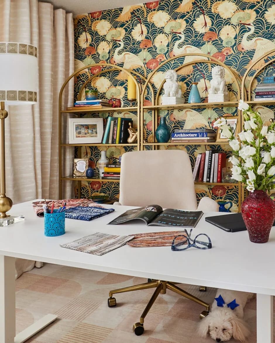 Modern home office with white desk, cream office chair, and brass shelving unit against a bold botanical wallpaper backdrop, designed by Nivi Ravi.