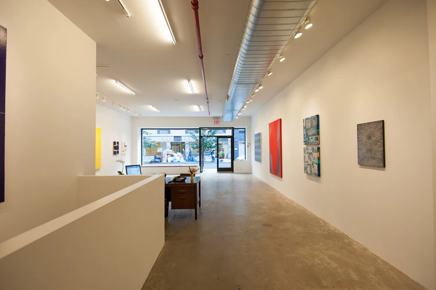 Minimalist gallery space with polished concrete floors, white walls, and track lighting displaying artwork installations by Niyati Singh.