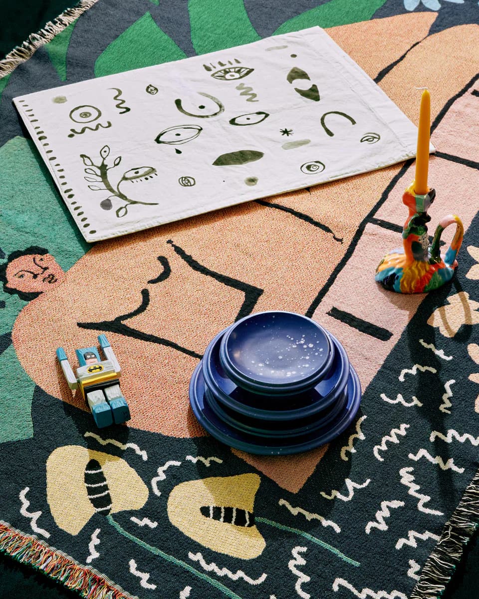 Styled flat lay arrangement featuring abstract paper sketches, a blue crystal ball, colorful candlestick, and patterned textiles in earthy and jewel tones by Noah Spencer.