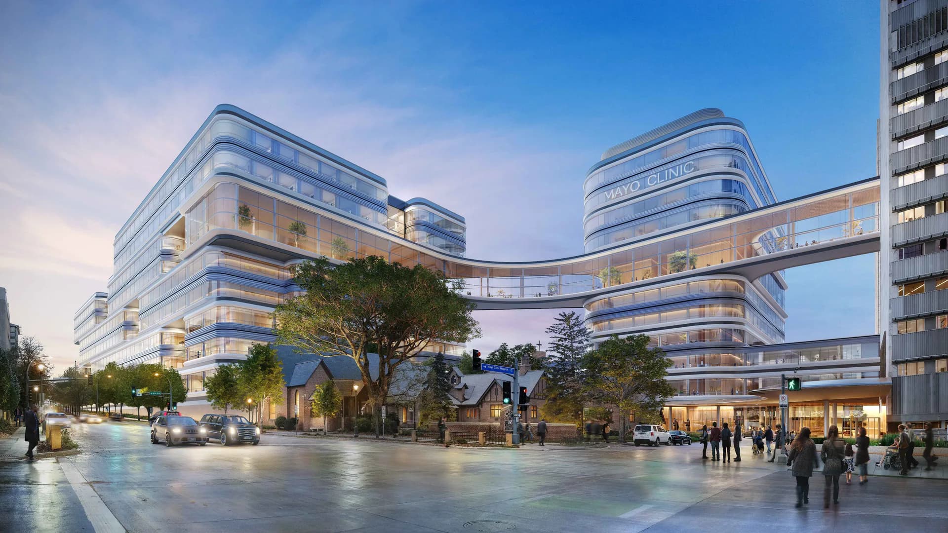 Curved modern plaza development with illuminated glass and metal facade featuring integrated retail spaces and pedestrian areas by Noah Waxman.