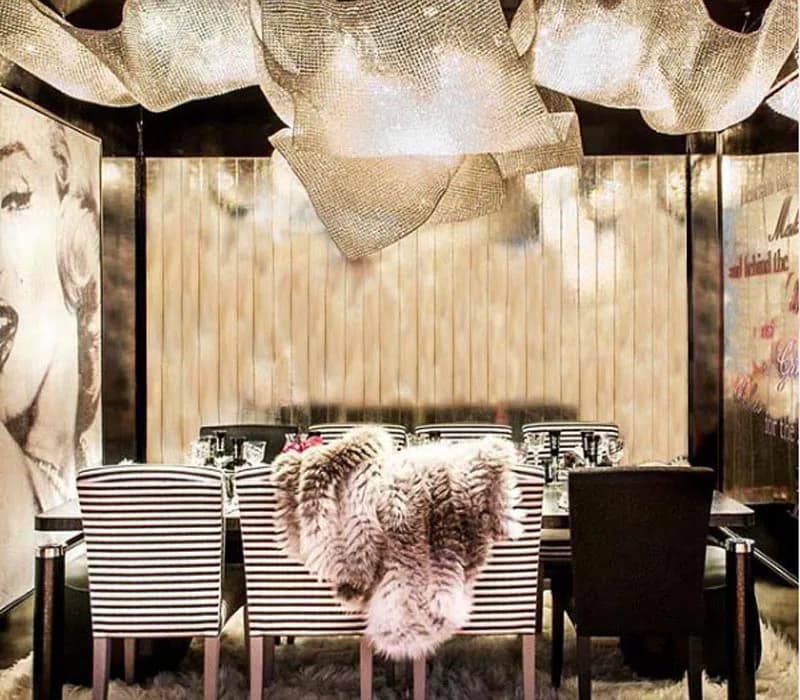 A luxury lounge interior with plush seating, dramatic overhead fabric installation, striped wall panels, and glamorous photography installations by Noelia Ibanez.