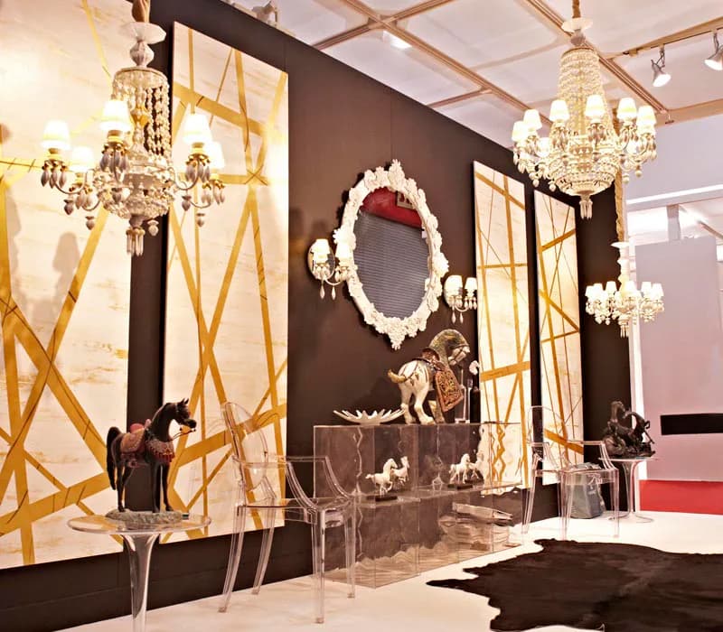 Luxe showroom interior with dark brown walls, gold geometric paneling, crystal chandeliers, and ornate oval mirror above a display case, designed by Noelia Ibanez.