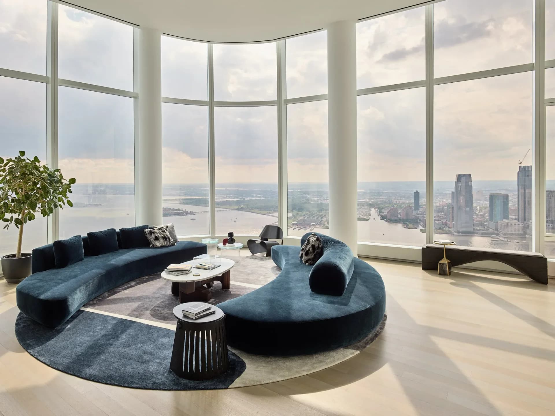 Curved blue modular seating arrangement in a high-rise penthouse with floor-to-ceiling windows overlooking a city skyline by Noha Hassan.