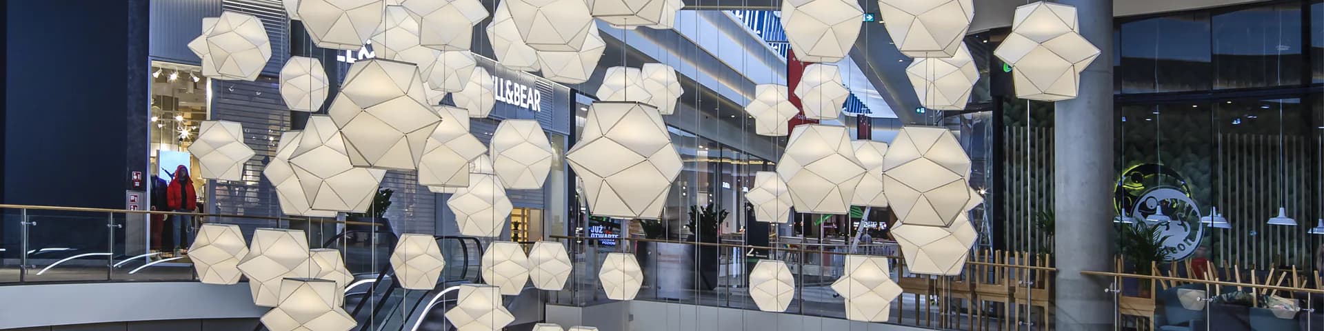 Modern lobby installation featuring suspended spherical white pendant lights arranged in a dynamic cluster above polished flooring and glass elements by Octavio Amado.