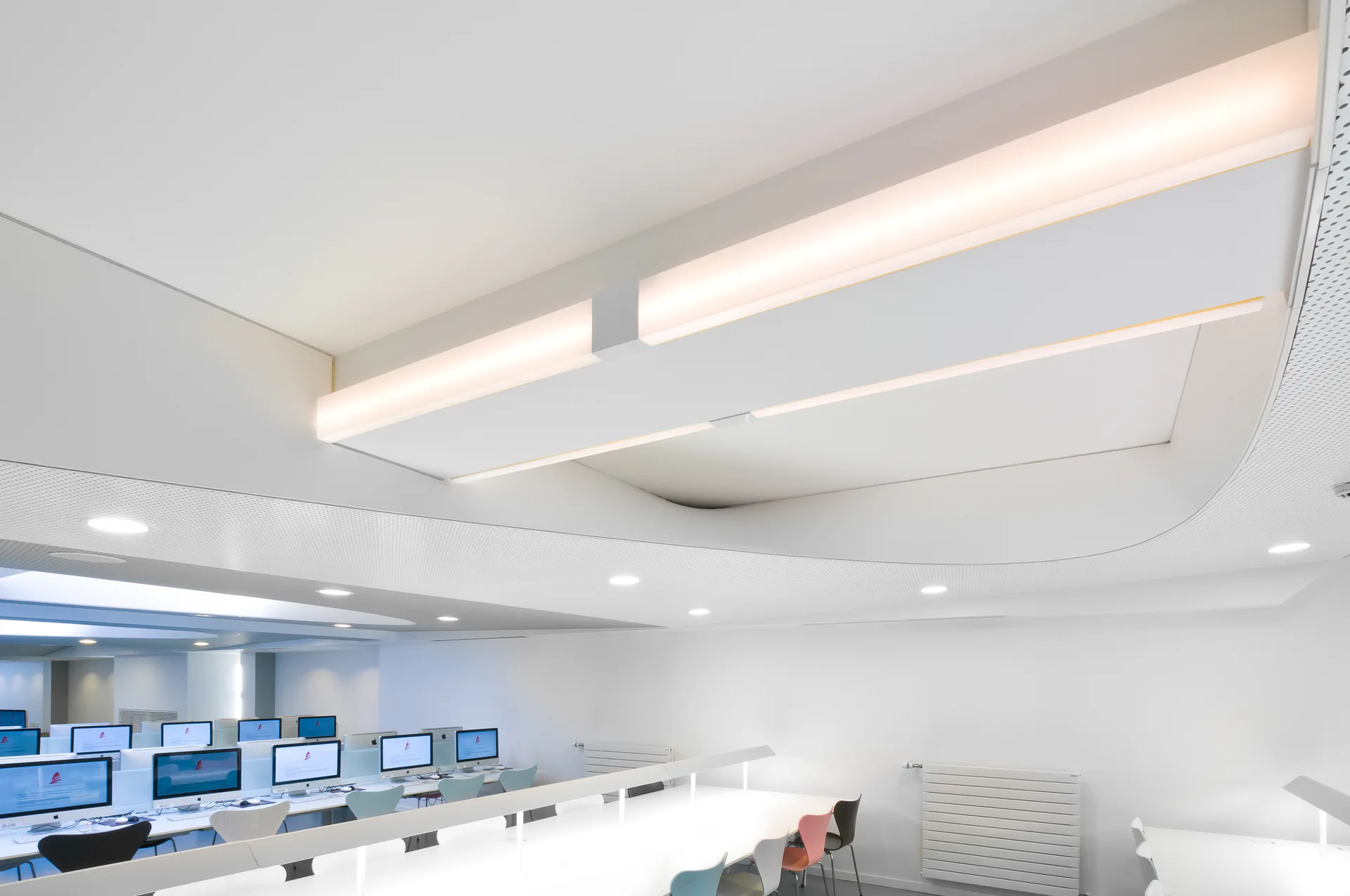 Modern control room with curved white ceiling, linear LED lighting, and workstations with multiple monitors along blue-accented walls by Octavio Amado.