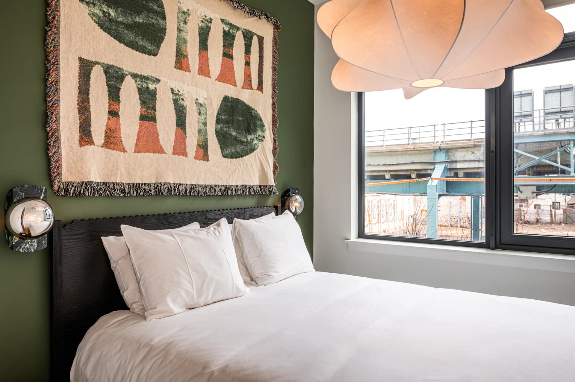 Modern bedroom with forest-green accent wall, white bedding, cloud pendant light, and geometric textile art above black headboard by Olivia Barry.