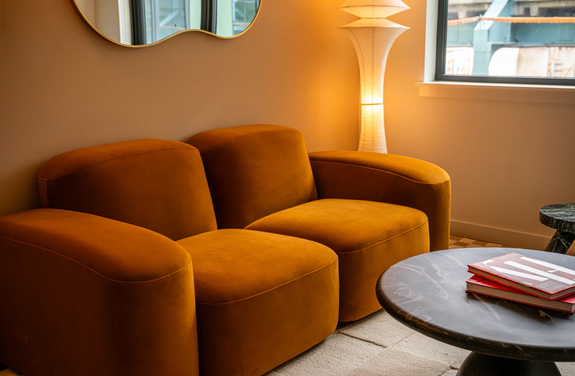 Warm ochre interior lounge featuring sculptural curved seating, marble-top side table, and ambient floor lamp by Olivia Barry.