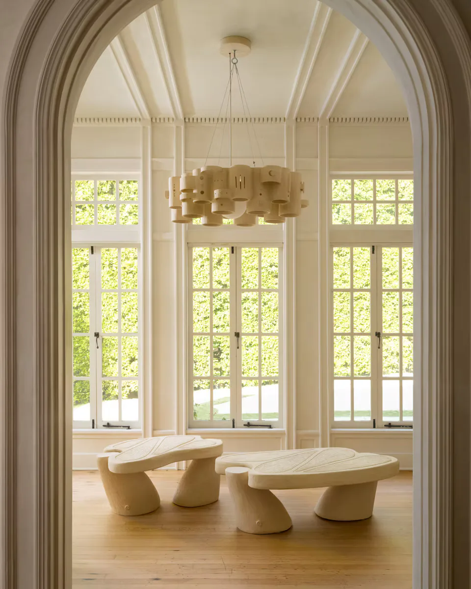 Minimalist interior with arched ceiling, natural light from tall windows, sculptural pendant fixture, and organic curved furniture in cream tones by Olivia Cognet.