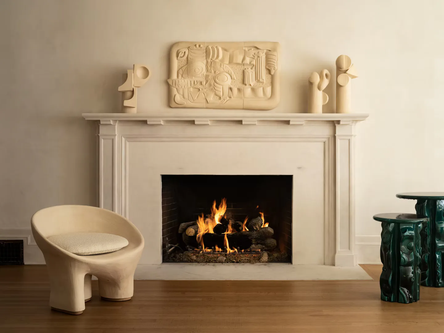 Cream-toned fireplace interior with sculptural furnishings, decorative relief panels, and a modern curved chair, designed by Olivia Cognet.