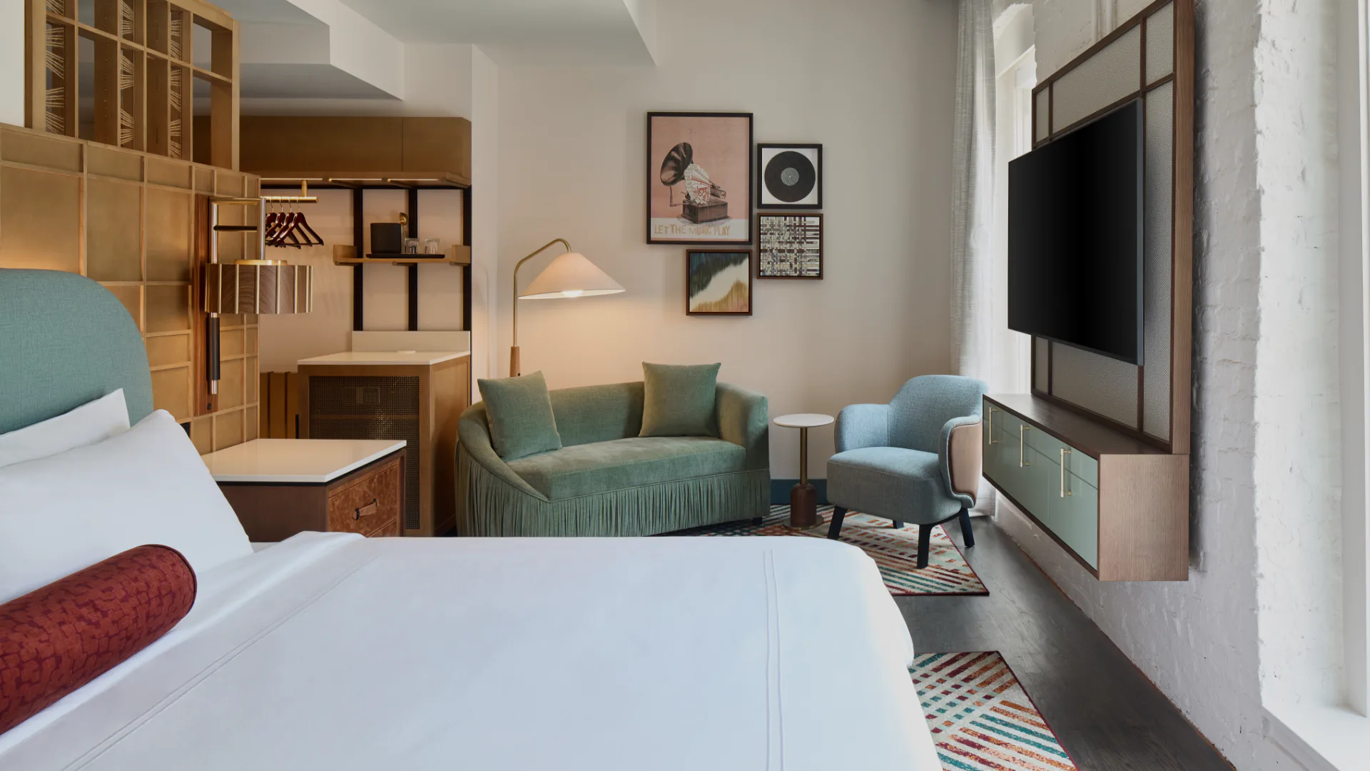 Modern hotel bedroom with wooden millwork, teal upholstered seating, and integrated media wall, designed by Olivia Cooper.