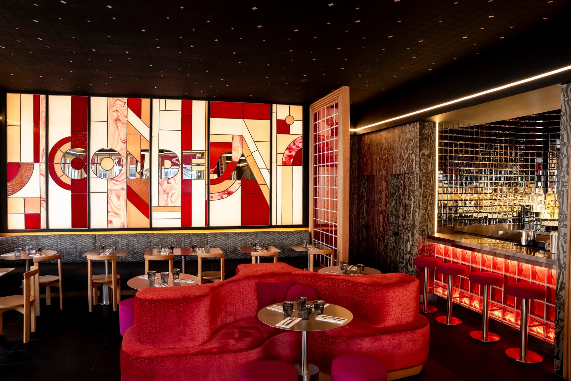 Modern lounge with red curved seating, geometric red and cream striped wall art, dark ceiling with ambient lighting, and wood accents by Pablo Castellanos.