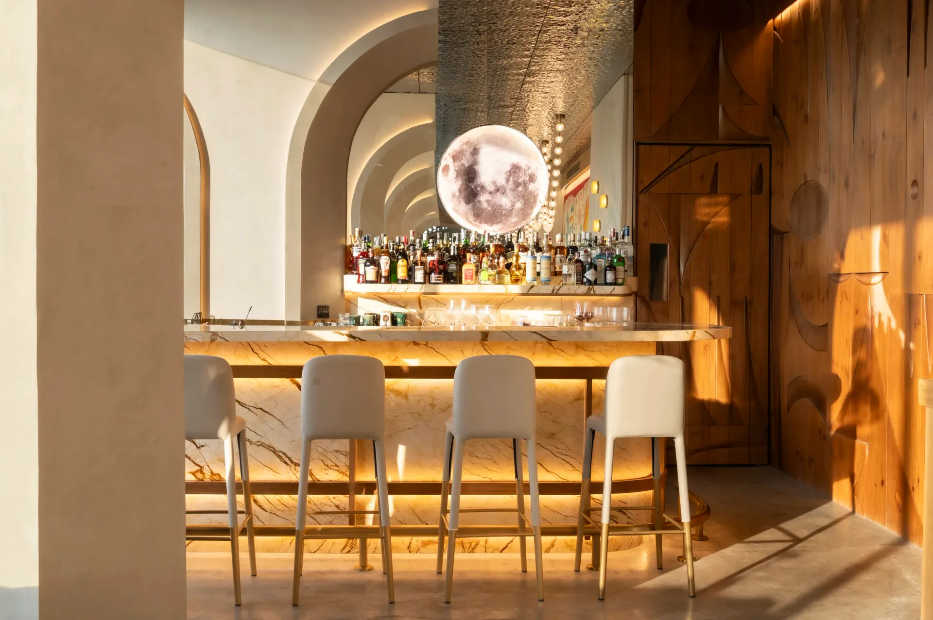 Modern bar interior with curved archways, backlit shelving, cream seating, and dramatic warm lighting designed by Pablo Castellanos.