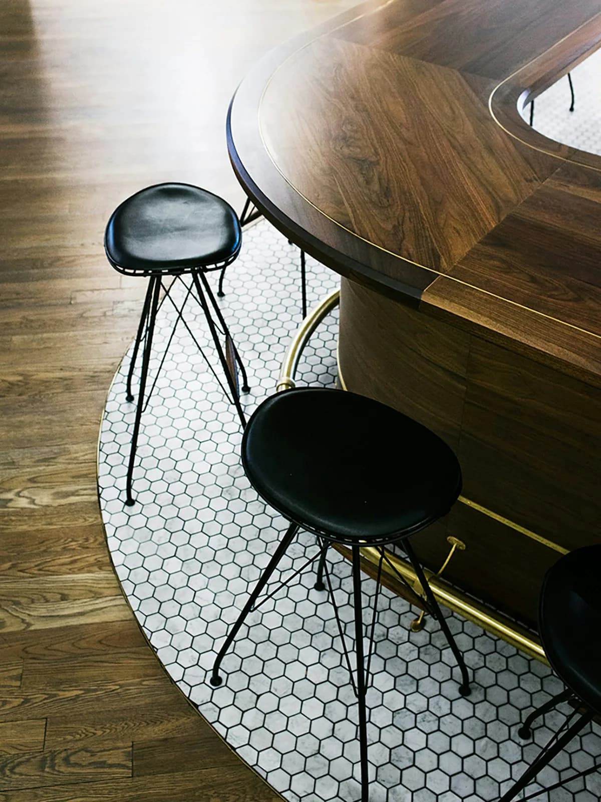 Modern bar seating with black metal stools and walnut curved counter overlooking white hexagonal tile flooring by Pam Chaiyachakorn.