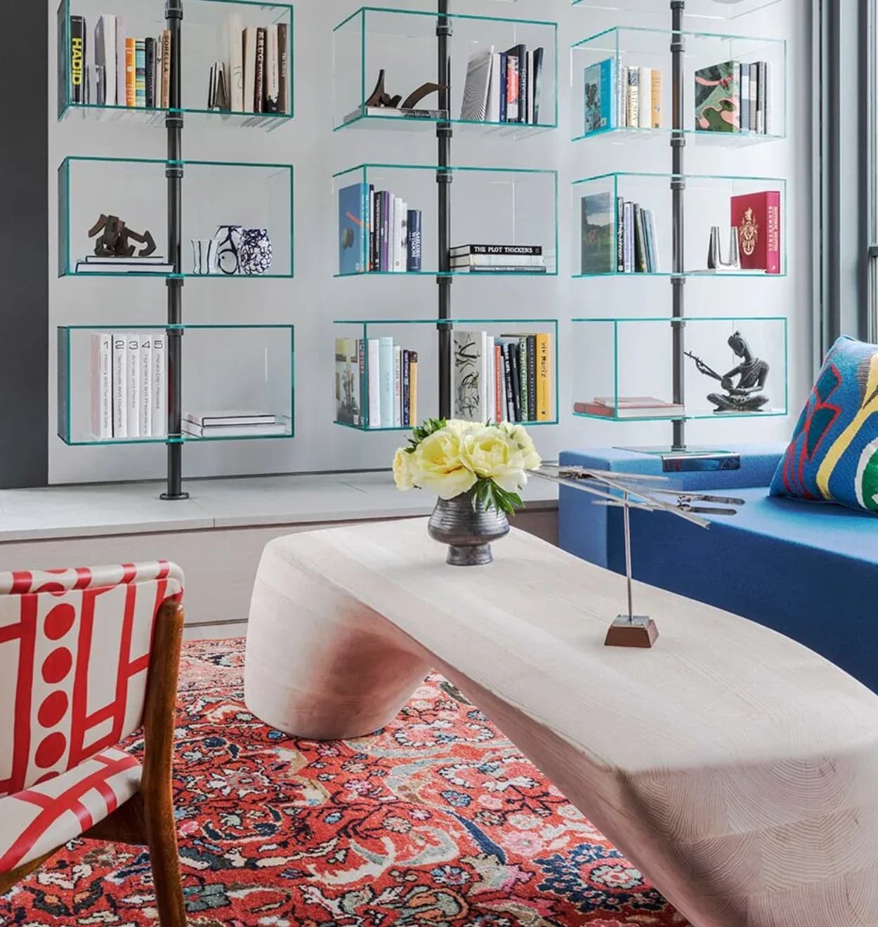 Modern living room with modular glass shelving, white curved furniture, colorful patterned rug, and blue sofa by Pamela R Ackerman.